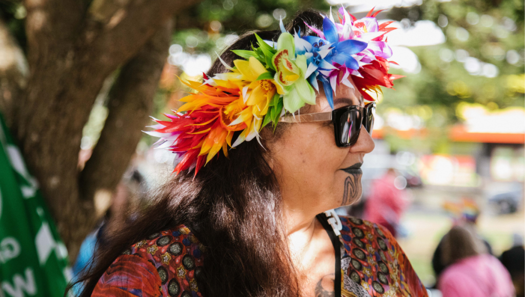 A picture of Elizabeth at Wellington Pride. She has a bright, Samoa sei (flower crown) in her head in the colours of the rainbow.